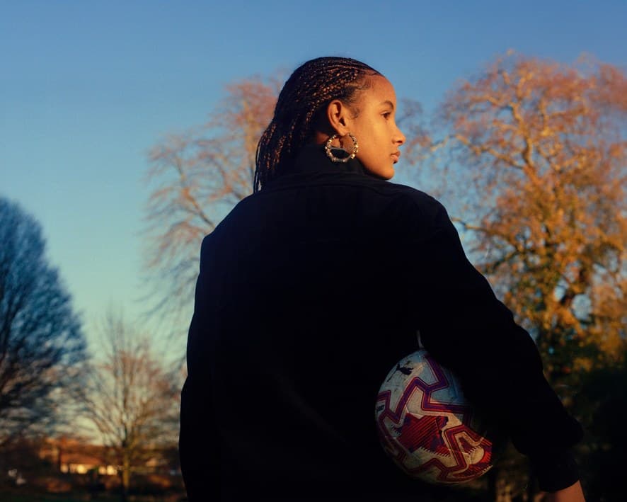 A woman at dusk holding a football against her hip