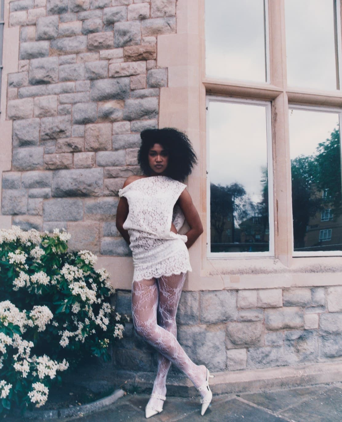 Woman in white lace standing against a stone house