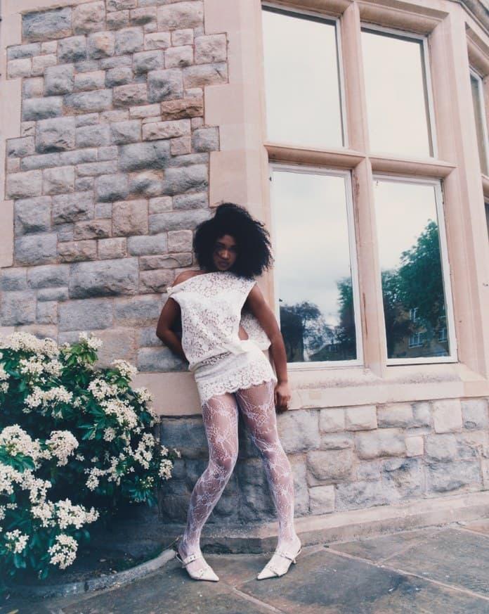 Woman in white lace leaning on a stone wall beside flowers