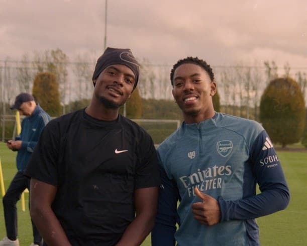 Two men smiling on the pitch, one in an Arsenal shirt